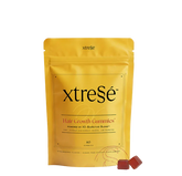 A yellow stand-up pouch of xtreSe Hair Growth Gummies with two small red gummies in front, photographed on a clean white background.