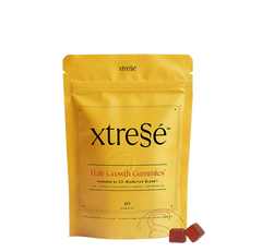 A yellow stand-up pouch of xtreSe Hair Growth Gummies with two small red gummies in front, photographed on a clean white background.